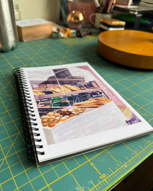 Sketchbook open to page with baked bread drawing, on a green cutting mat