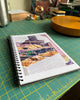 Sketchbook open to page with baked bread drawing, on a green cutting mat