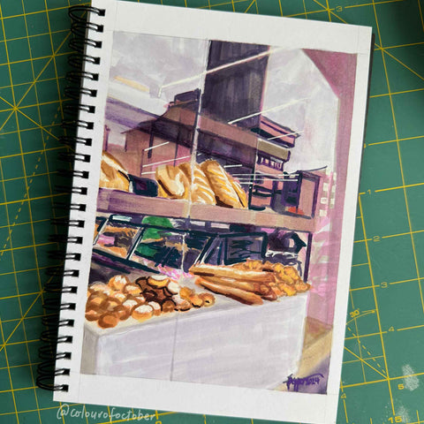 Sketchbook open to a page with a marker drawing of a bakery, on a green cutting mat