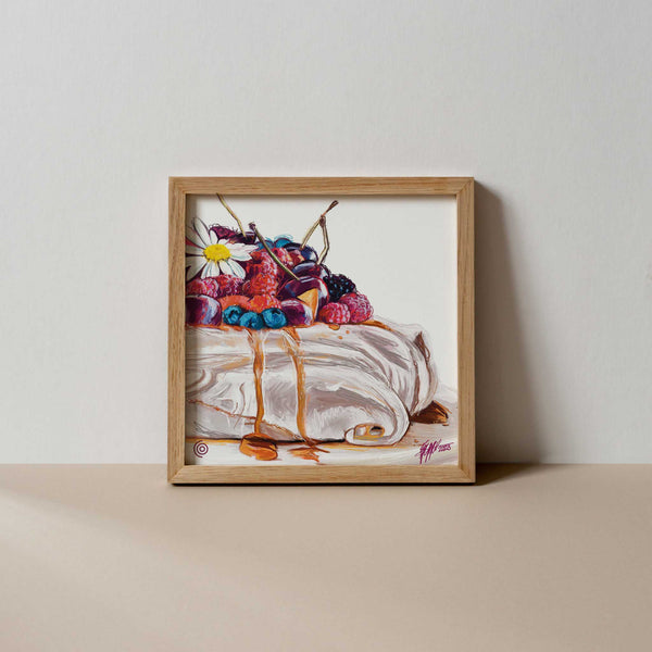 A colourful fine art print of a digital painting featuring a pavlova dessert topped with a white and yellow flower, berries, cream, and syrup, in a light brown frame, against a neutral background. 